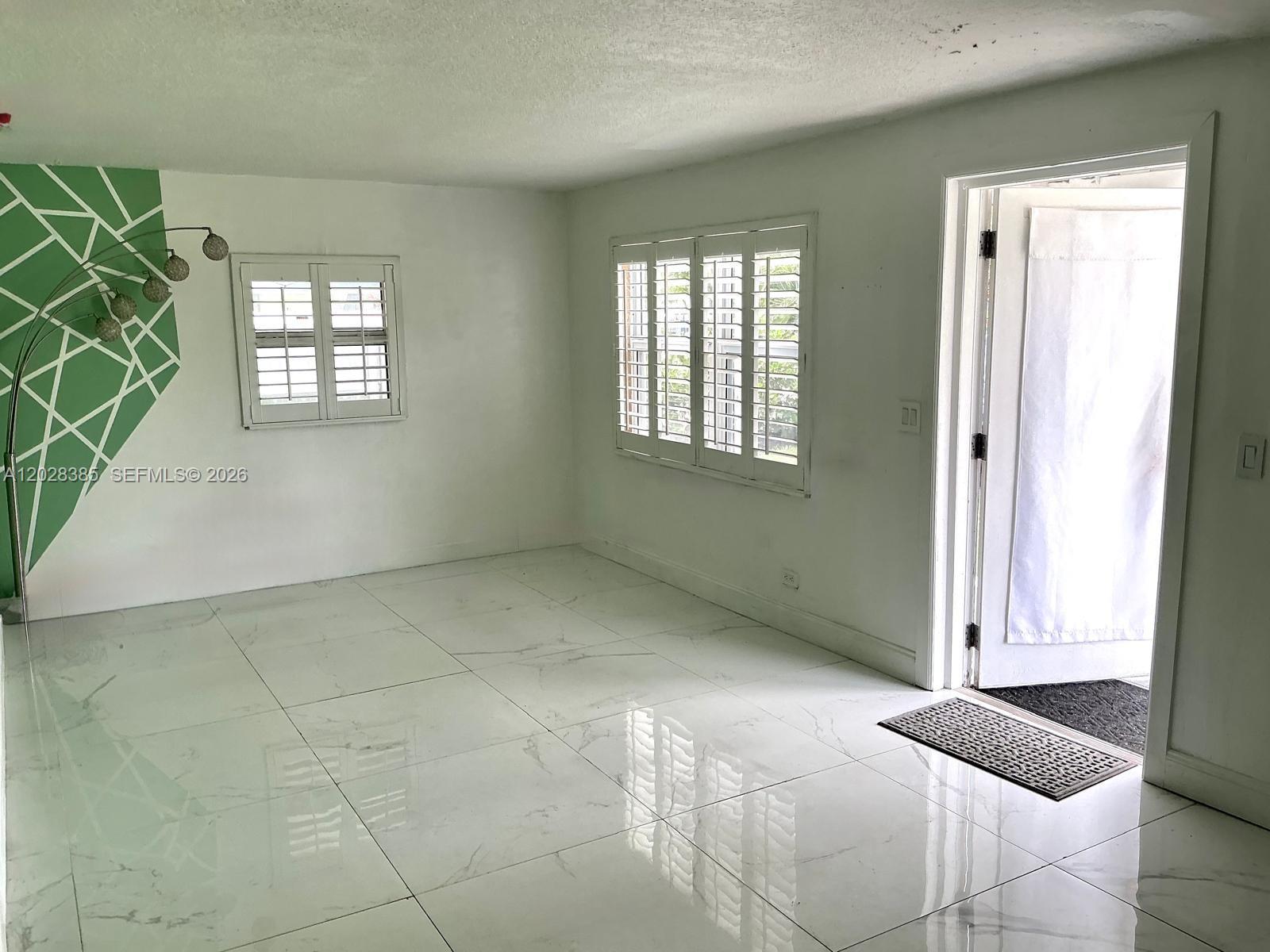 A bright room features white marble-look tile floors, plantation shutters, and a geometric green accent wall — 6025 SW 40th St, Miramar FL 33023, MIRAMAR, FL