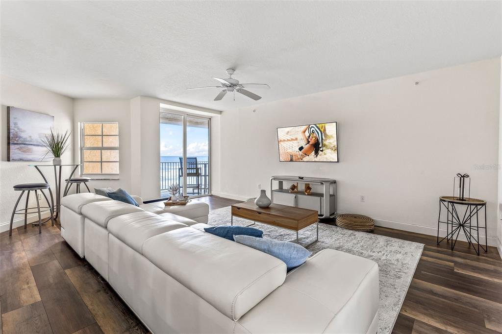 A living room features a white sectional sofa, wood flooring, and a balcony overlooking the ocean — 3145 S ATLANTIC AVENUE UNIT 405, DAYTONA BEACH SHORES, FL
