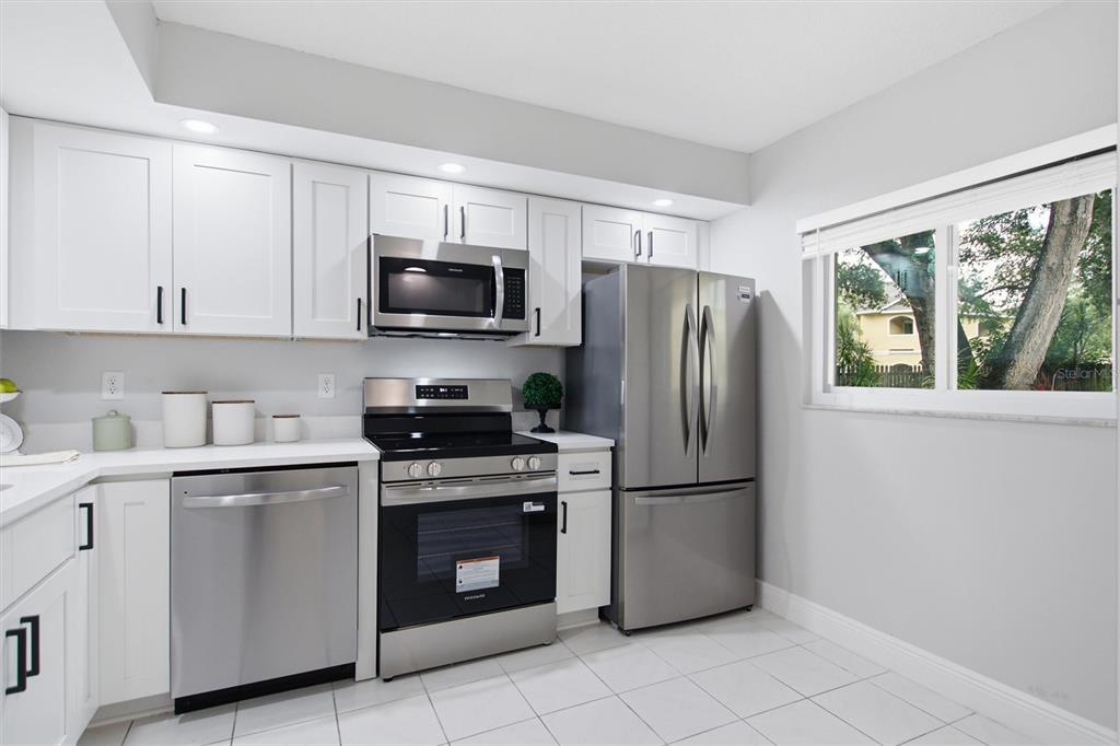 A kitchen features white cabinets, stainless steel appliances, and white tile flooring — 1241 S MARTIN LUTHER KING JR AVENUE UNIT 104, CLEARWATER, FL