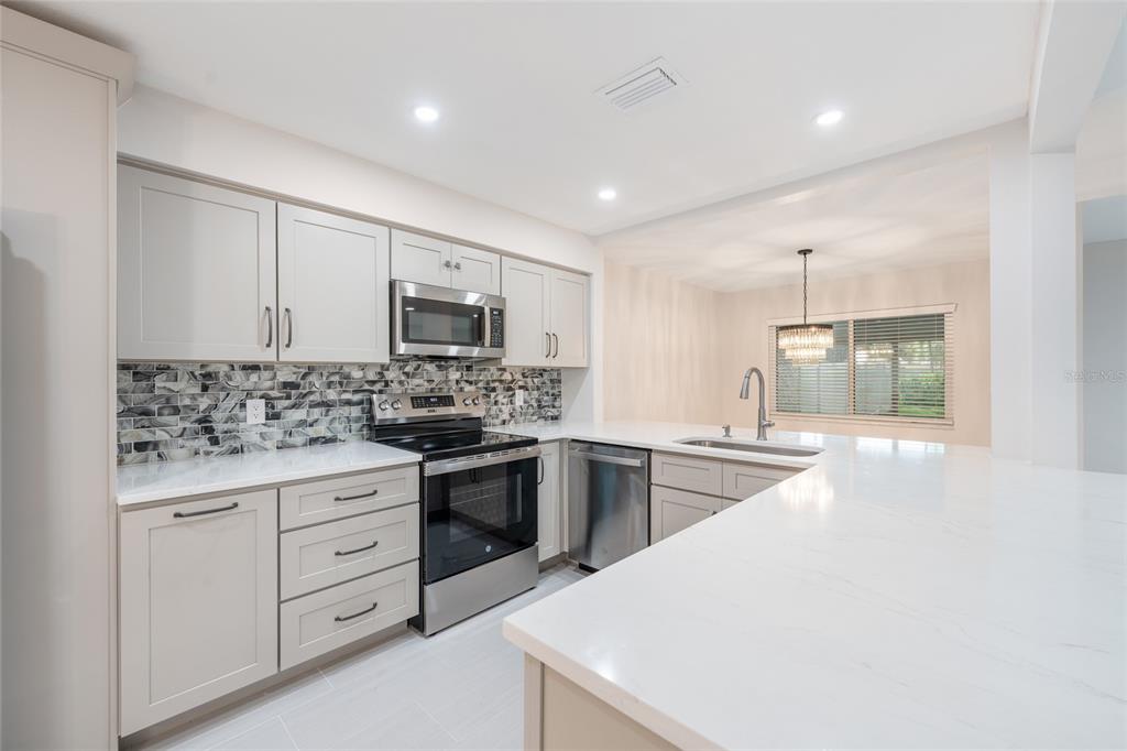 A modern kitchen features light gray cabinets, white quartz countertops, stainless steel appliances, and tile backsplash — 8137 CITRUS CHASE DRIVE, ORLANDO, FL