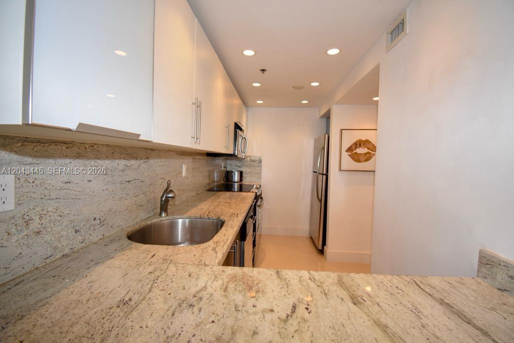A galley kitchen features white cabinets, granite countertops, a stainless steel sink, and stainless appliances — 100 Lincoln Rd # 1507, Miami Beach FL 33139, MIAMI BEACH, FL