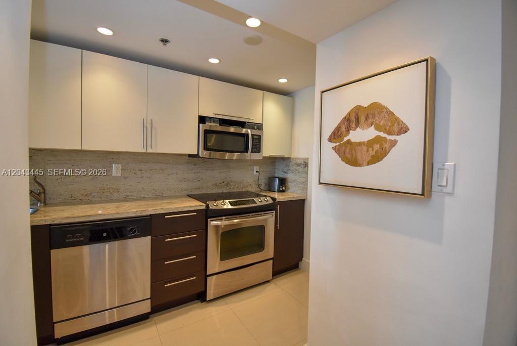 A kitchen features white upper cabinets, dark lower cabinets, stainless steel appliances, and granite countertops — 100 Lincoln Rd # 1507, Miami Beach FL 33139, MIAMI BEACH, FL