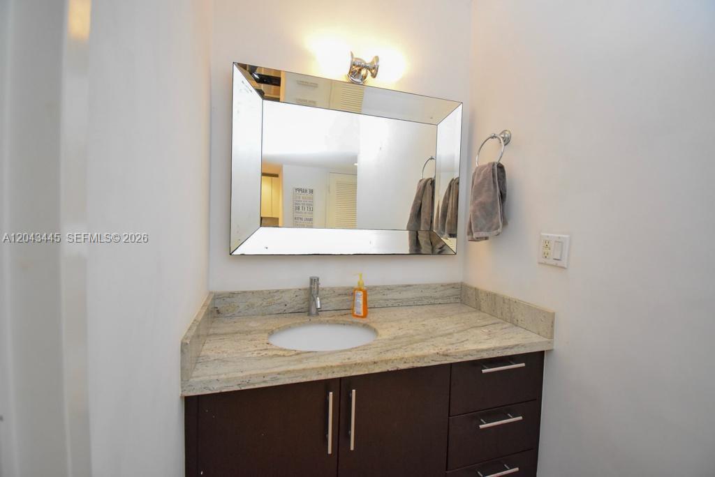 A bathroom vanity features a dark wood cabinet, granite countertop, and a rectangular wall mirror — 100 Lincoln Rd # 1507, Miami Beach FL 33139, MIAMI BEACH, FL