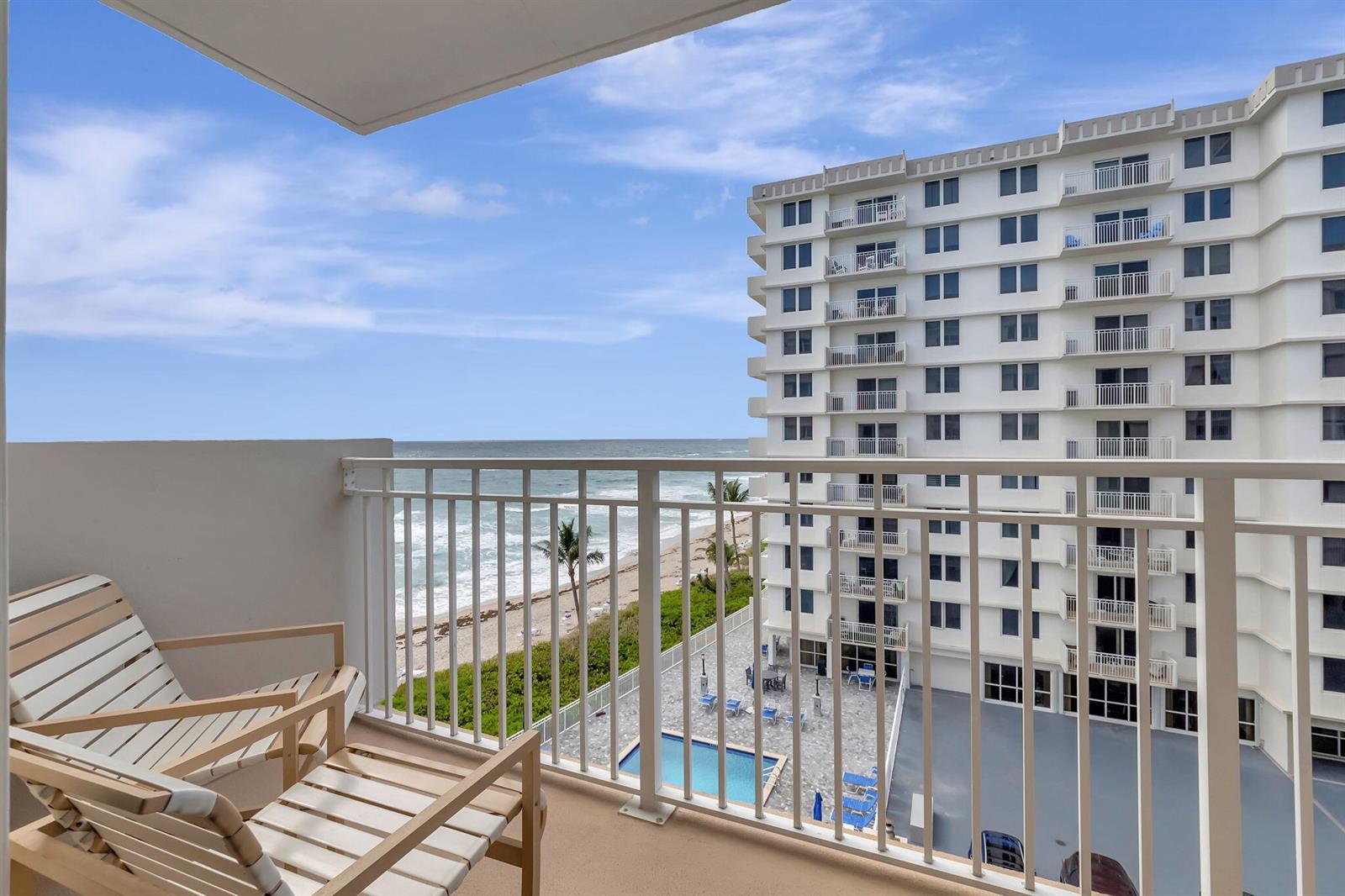 A balcony with two chairs overlooks a beach, the ocean, and a neighboring apartment building — 3215 S Ocean Boulevard # 509, Highland Beach FL 33487, HIGHLAND BEACH, FL