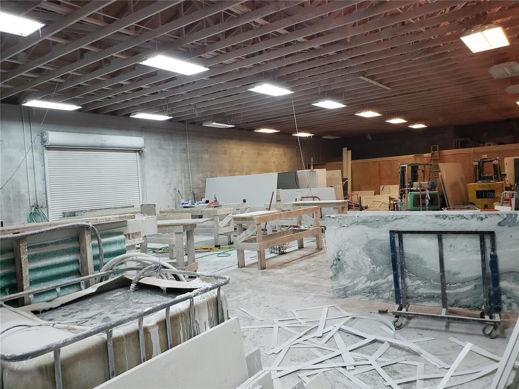 An industrial workshop space features exposed ceiling beams, fluorescent lighting, and stone slab storage racks — 5010 N GRADY AVENUE, TAMPA, FL