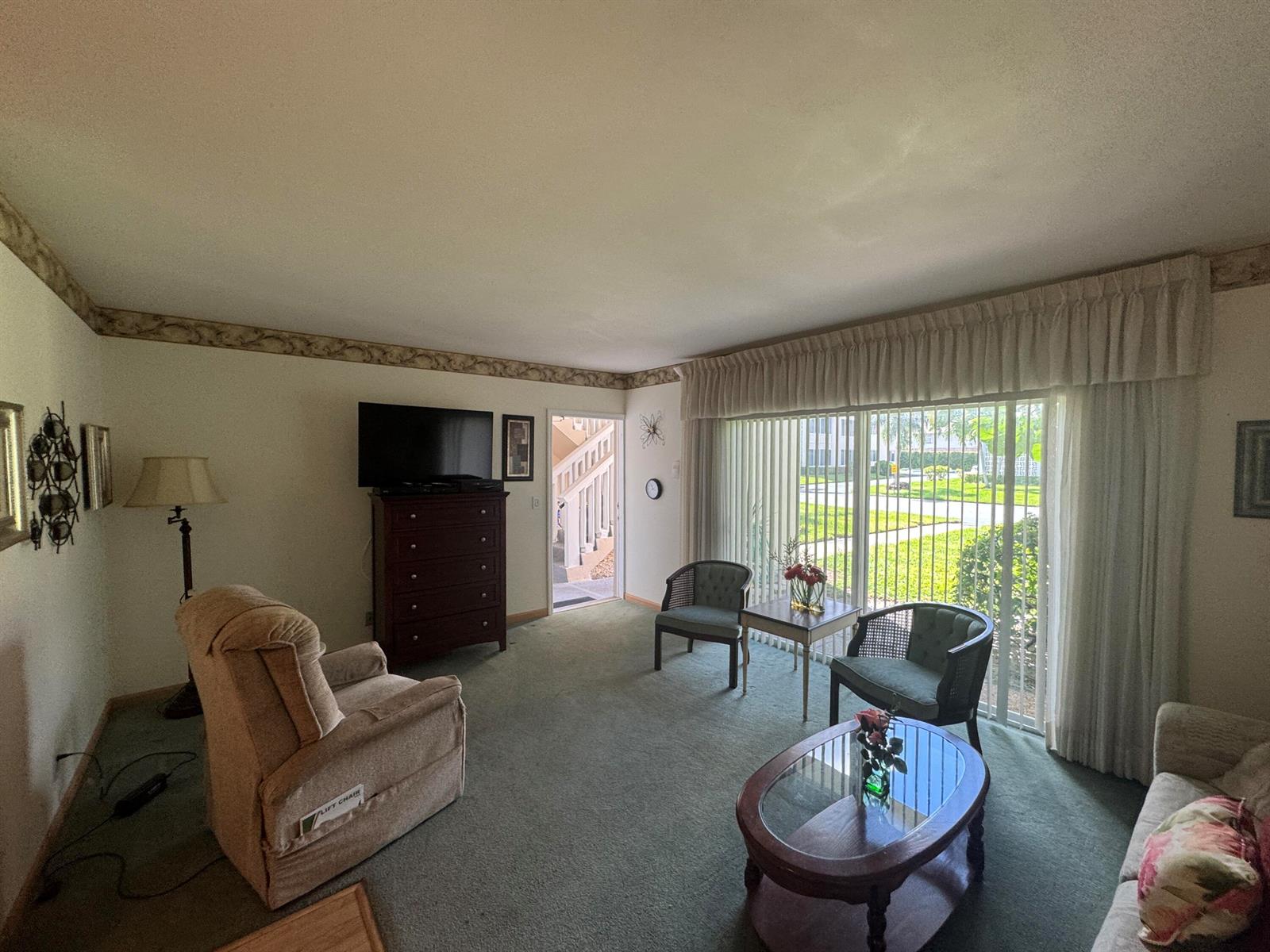 A living room features green carpeting, a television on a dresser, and a sliding glass door — 115 S South Boulevard # 1c, Boynton Beach FL 33435, BOYNTON BEACH, FL