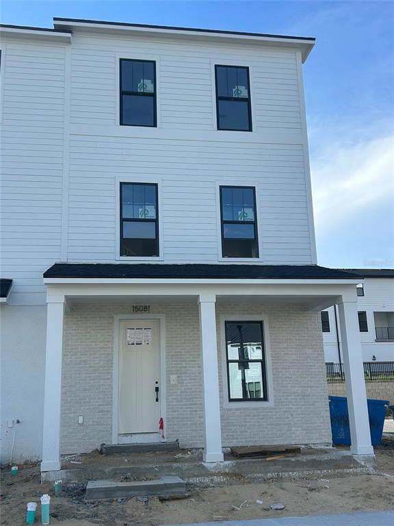 A three-story townhouse exterior features white horizontal siding, a brick facade, and a covered porch — 15081 GROVESIDE ROAD, WINTER GARDEN, FL