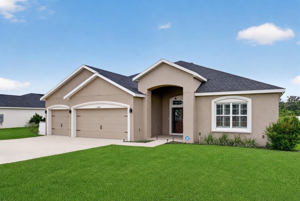 A single-story beige stucco house with a three-car garage and a front entryway — 9074 SE 48TH COURT ROAD, OCALA, FL