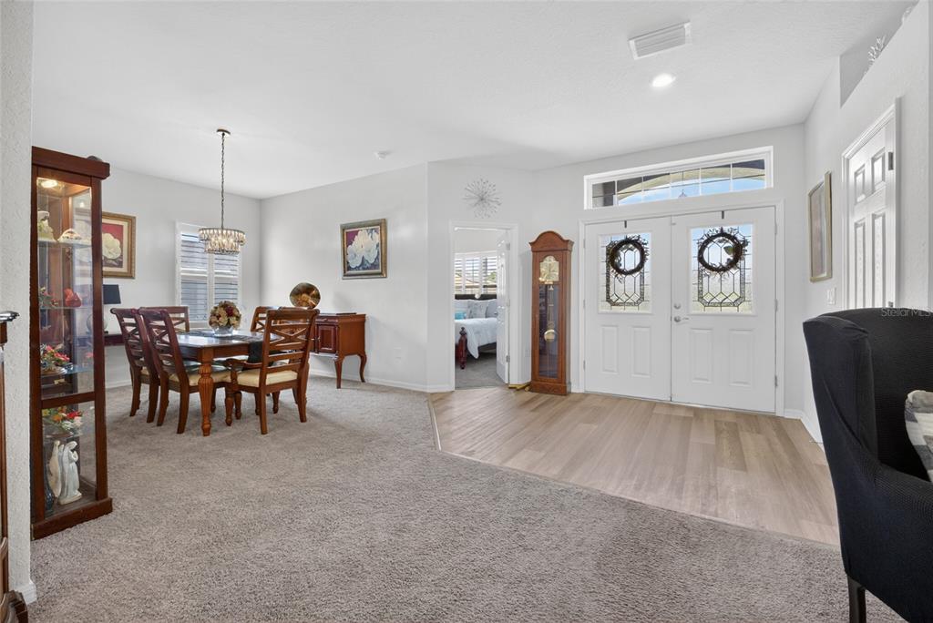 An entryway with wood-look flooring leads into a carpeted dining room with a grandfather clock — 9074 SE 48TH COURT ROAD, OCALA, FL