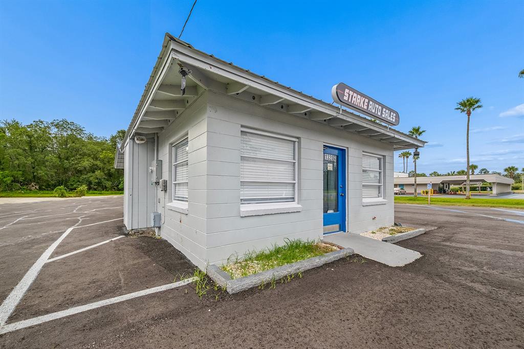 A small, gray, single-story commercial building with a blue door sits on an asphalt lot — 1320 N TEMPLE AVENUE, STARKE, FL