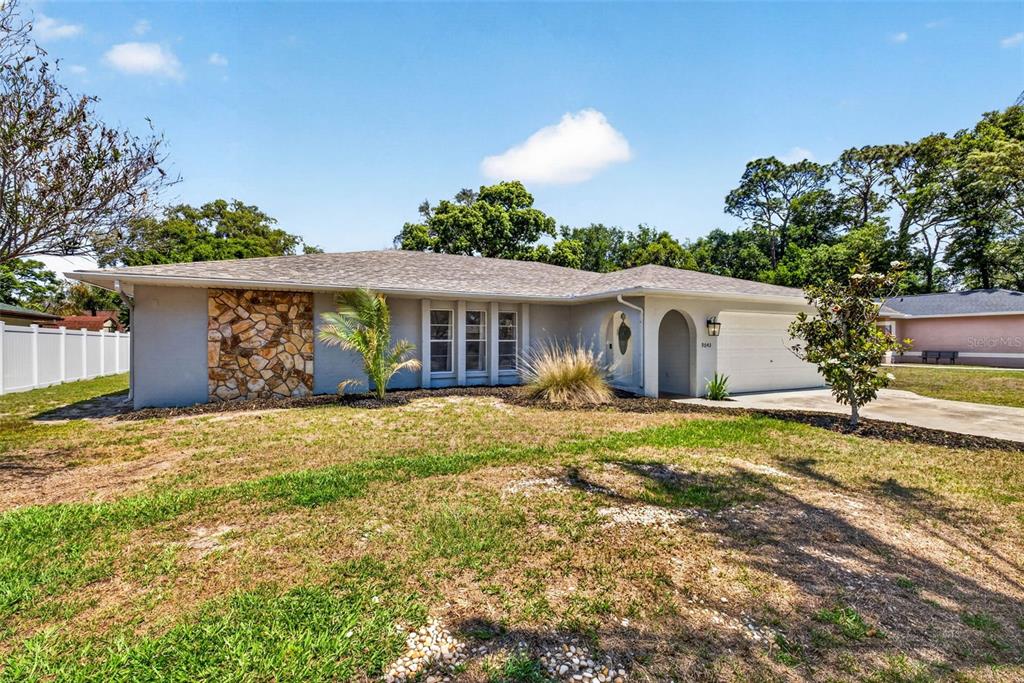 A single-story house with a stone facade, a white garage, and a large front lawn — 9043 MCCORMICK STREET, SPRING HILL, FL
