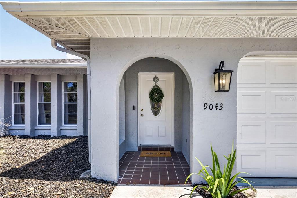 The exterior of a house features a white arched entryway, a front door, and a garage — 9043 MCCORMICK STREET, SPRING HILL, FL