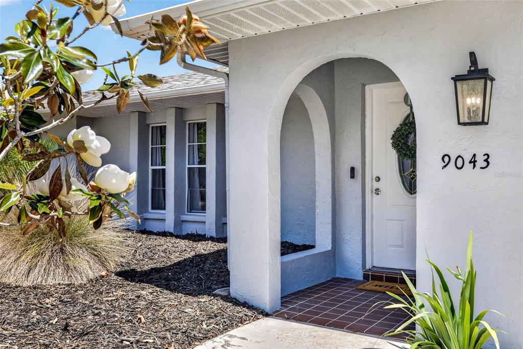 A white house exterior features an arched entryway, a white front door, and dark mulch — 9043 MCCORMICK STREET, SPRING HILL, FL