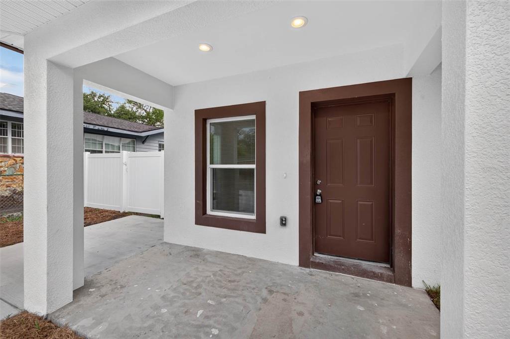 A covered concrete porch features a brown front door and a window with brown trim — 3420 N 10TH STREET, TAMPA, FL