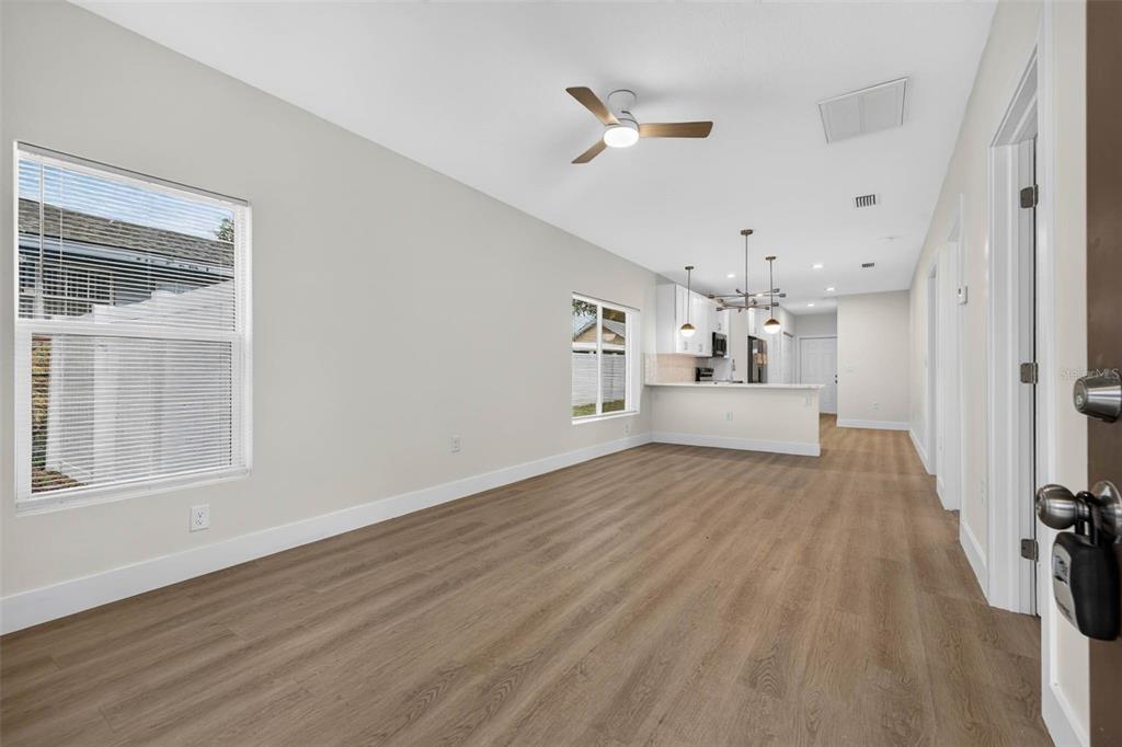 An open-concept living area features light wood-look flooring, white walls, and a kitchen in the background — 3420 N 10TH STREET, TAMPA, FL