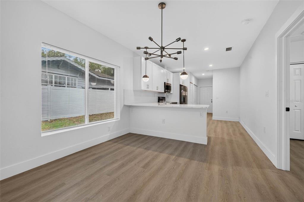 A bright kitchen and dining area feature white cabinets, a breakfast bar, and wood-look flooring — 3420 N 10TH STREET, TAMPA, FL