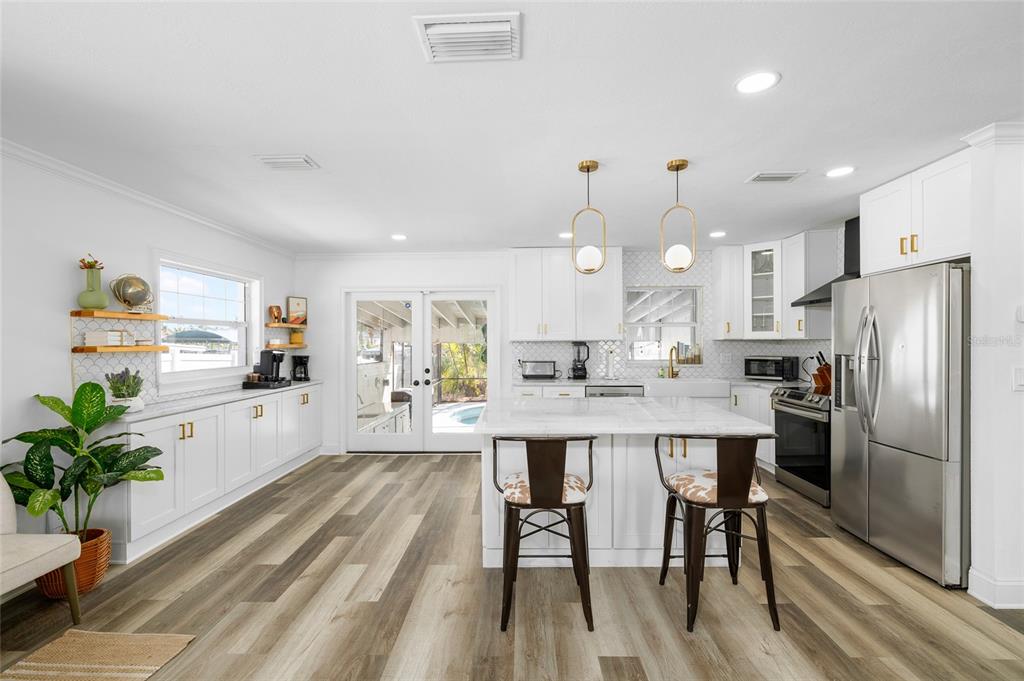 A bright, modern kitchen features white cabinetry, a marble-topped island, and wood-look flooring — 10716 DONBRESE AVENUE, TAMPA, FL