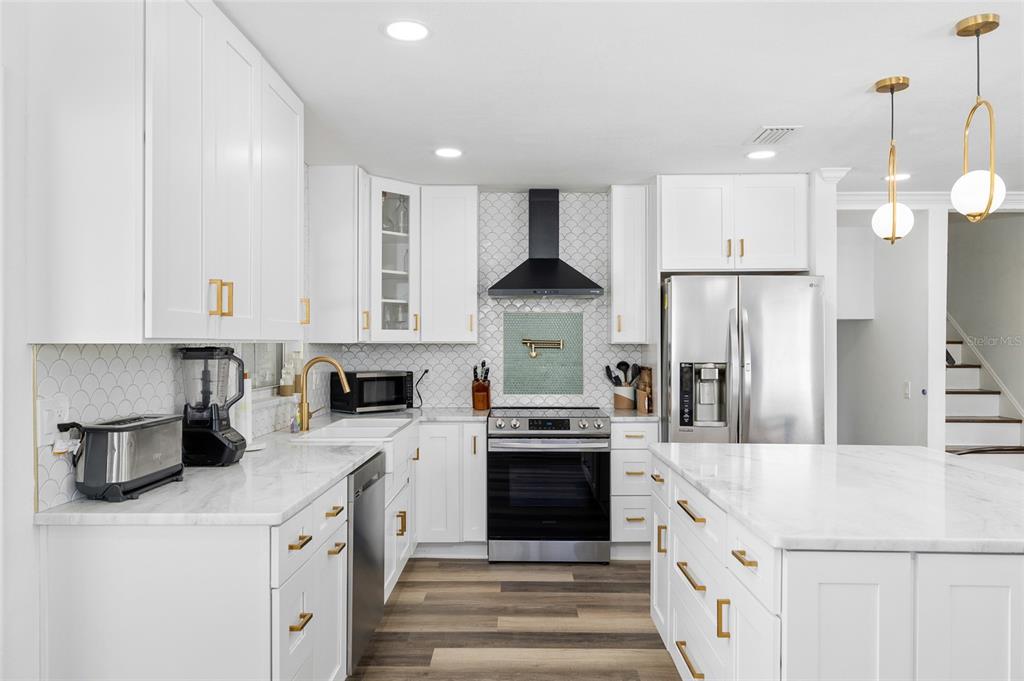 A modern kitchen features white cabinets, marble countertops, stainless steel appliances, and a tiled backsplash — 10716 DONBRESE AVENUE, TAMPA, FL