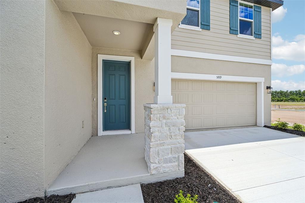 The exterior of a two-story home features a teal front door, stone pillar, and garage — 5919 FRESH FLORA DRIVE, WIMAUMA, FL