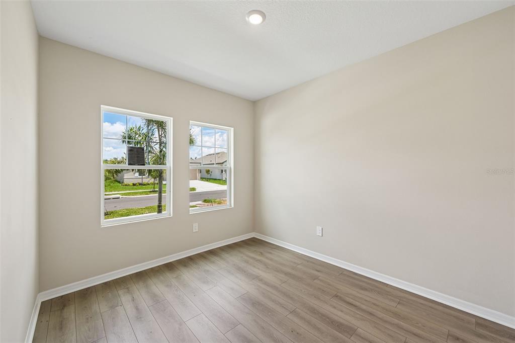An empty room with light-colored walls, wood-look flooring, and two windows overlooking a street — 5919 FRESH FLORA DRIVE, WIMAUMA, FL