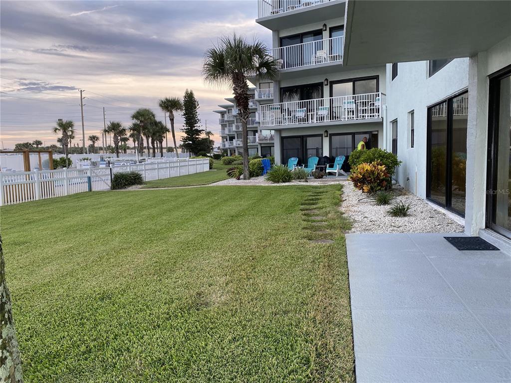 A grassy lawn leads to a multi-story building with balconies and patio seating — 1571 S ATLANTIC AVENUE UNIT 108, NEW SMYRNA BEACH, FL
