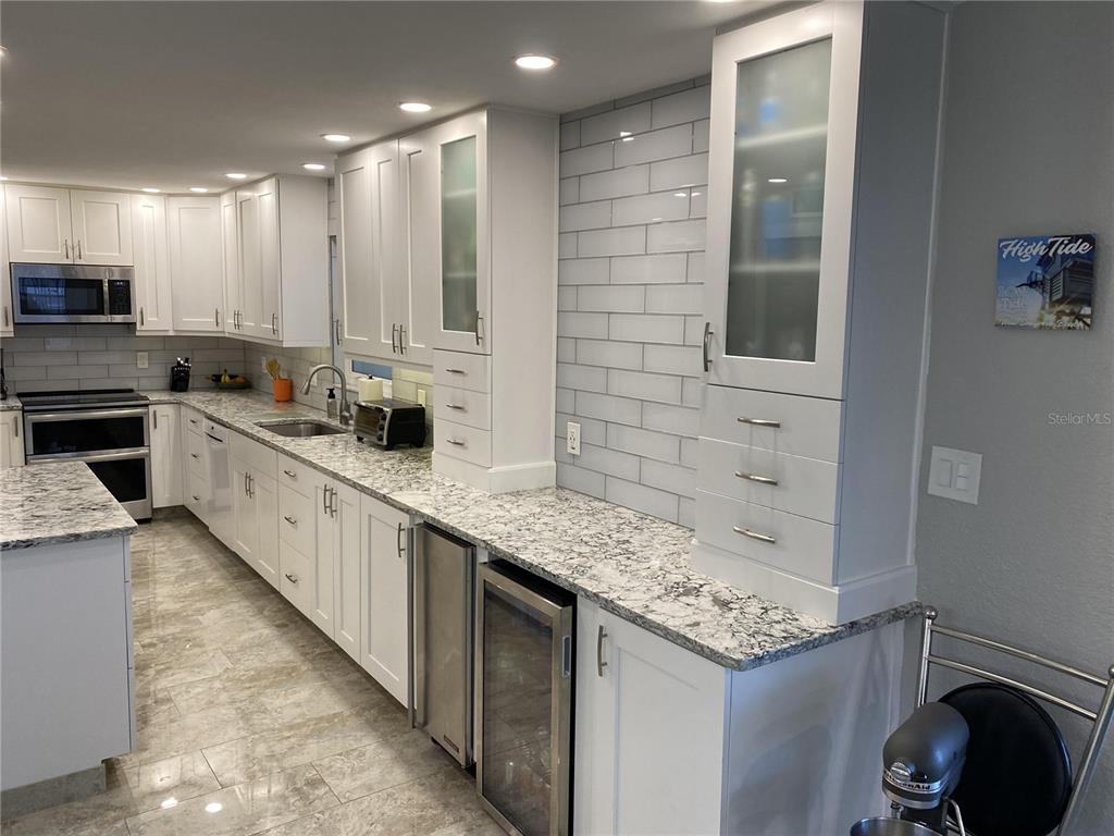 A kitchen features white cabinets, granite countertops, stainless steel appliances, and gray subway tile backsplashes — 1571 S ATLANTIC AVENUE UNIT 108, NEW SMYRNA BEACH, FL