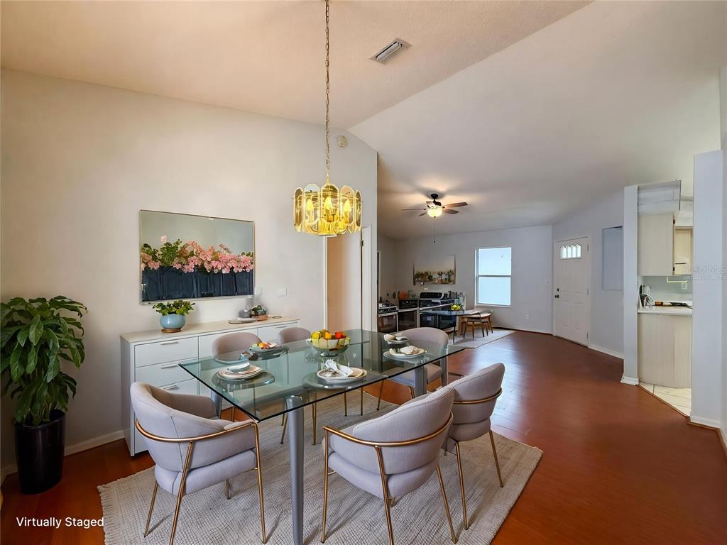A dining area with a glass table, upholstered chairs, and a gold chandelier on hardwood floors — 5507 LAVER STREET, LEESBURG, FL