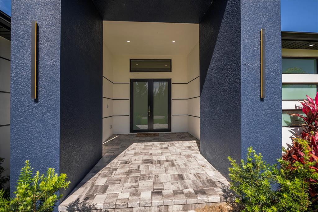 A modern entryway features a dark blue stucco exterior, double glass doors, and paver flooring — 9493 ST PAUL DRIVE, PORT CHARLOTTE, FL