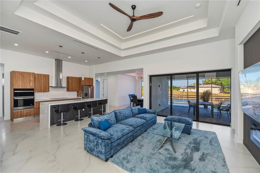 A modern open-concept living room and kitchen feature a blue sofa, marble floors, and sliding doors — 9493 ST PAUL DRIVE, PORT CHARLOTTE, FL