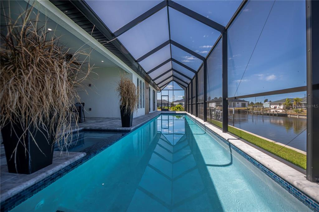A narrow lap pool with an attached spa sits inside a screened-in patio by water — 9493 ST PAUL DRIVE, PORT CHARLOTTE, FL
