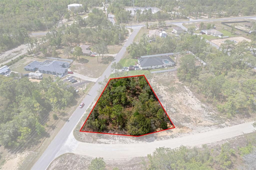 An aerial view shows a wooded, trapezoidal vacant lot outlined in red at a road intersection — 12140 MISSISSIPPI KITE AVENUE, BROOKSVILLE, FL