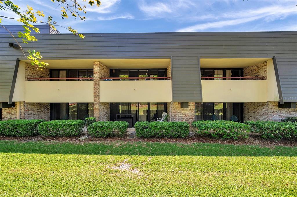 A two-story apartment building features brick accents, dark horizontal siding, and ground-level patio access — 36750 US 19 N UNIT 2763, PALM HARBOR, FL