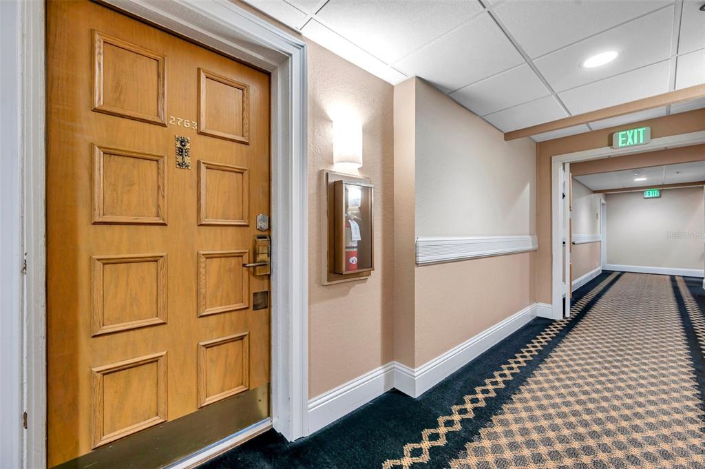 A hallway features a wooden door labeled 2763, a wall-mounted fire extinguisher, and carpeted flooring — 36750 US 19 N UNIT 2763, PALM HARBOR, FL