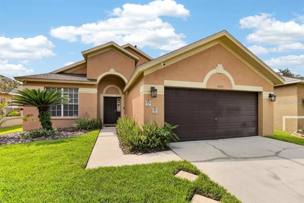 A tan, single-story suburban house features a two-car garage and a front entryway — 5605 HAWKLAKE ROAD, LITHIA, FL