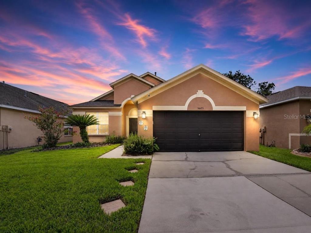 A single-story house with a tan stucco exterior, a black garage door, and a lawn — 5605 HAWKLAKE ROAD, LITHIA, FL