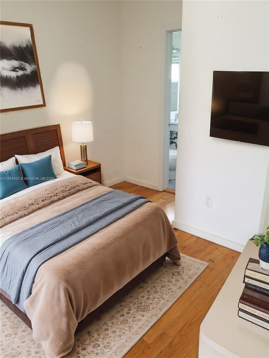 A bedroom features a bed with blue pillows, a wall-mounted television, and hardwood flooring — 745 13th St # 16, Miami Beach FL 33139, MIAMI BEACH, FL