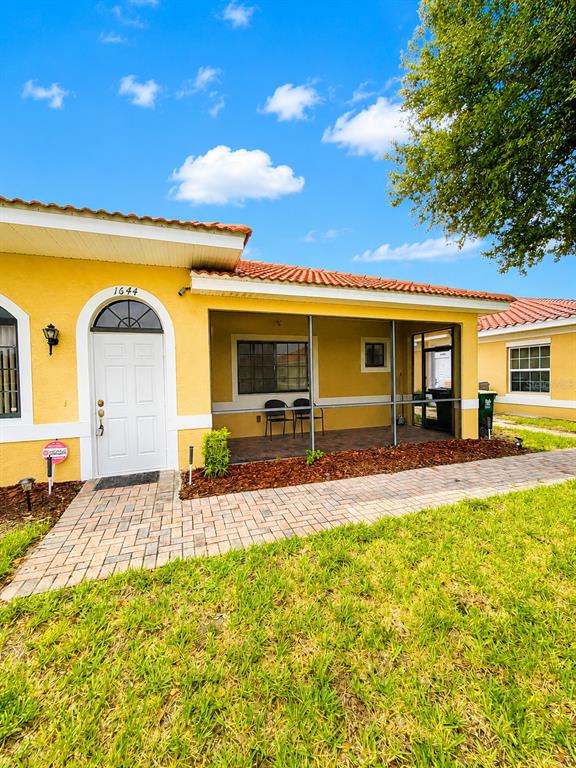 A yellow house with a screened-in porch and a brick walkway under a blue sky — 1644 CUMIN DRIVE, POINCIANA, FL