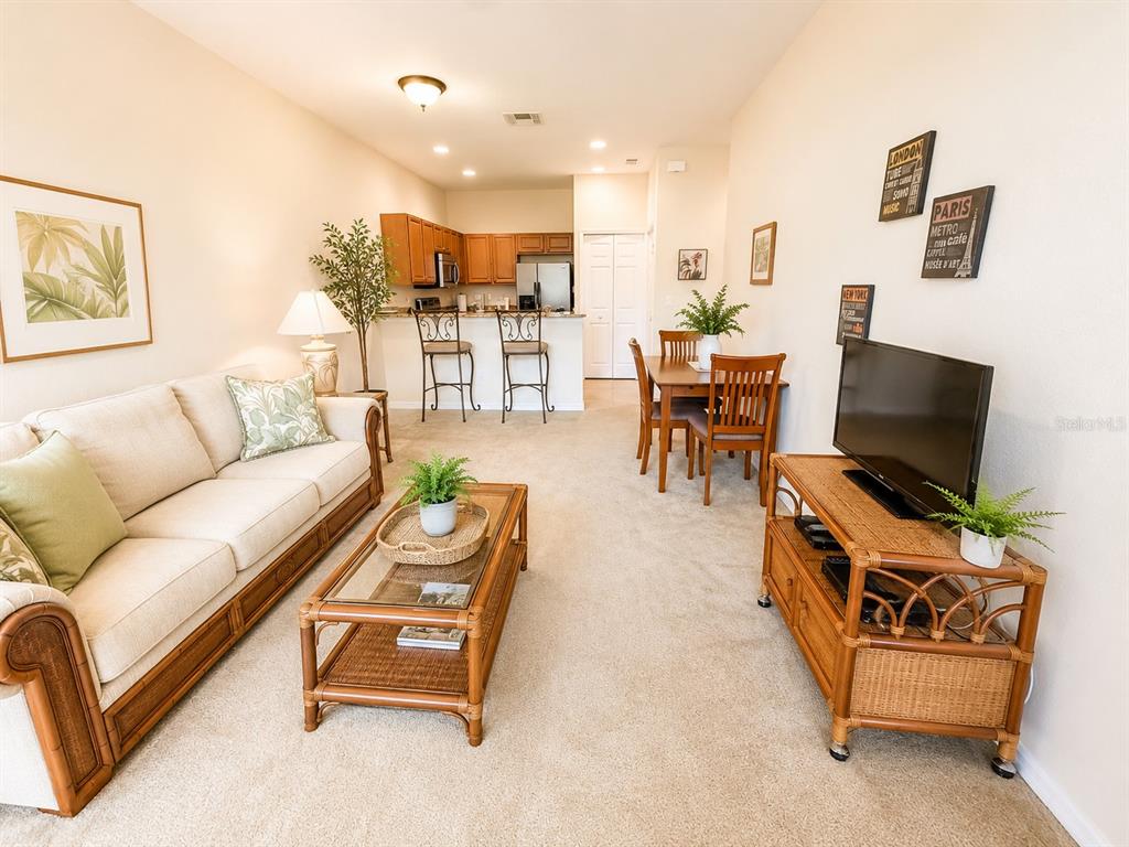 A living room with beige carpet, a rattan coffee table, and an open kitchen background — 1644 CUMIN DRIVE, POINCIANA, FL