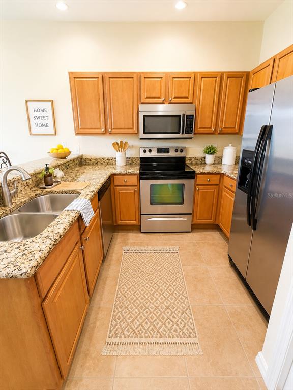 A kitchen features wood cabinets, granite countertops, stainless steel appliances, and a tiled floor — 1644 CUMIN DRIVE, POINCIANA, FL