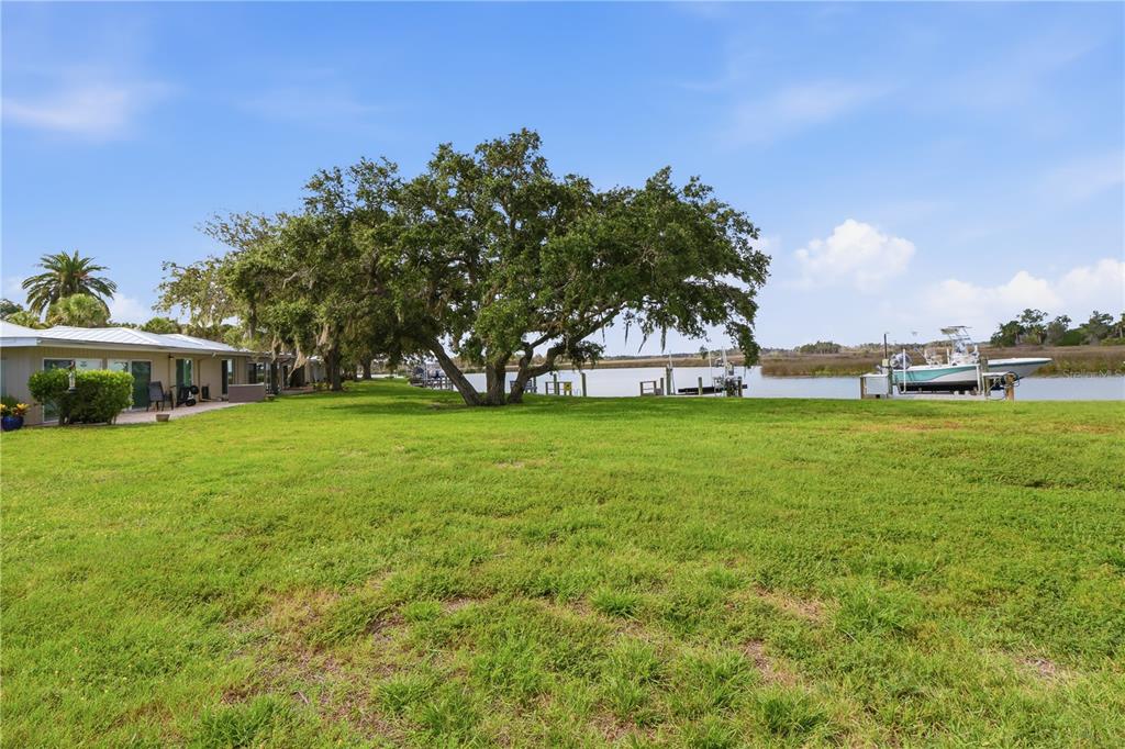 A grassy backyard leads to a large oak tree, a boat dock, and a waterway — 11628 W BAYSHORE DRIVE UNIT 8, CRYSTAL RIVER, FL