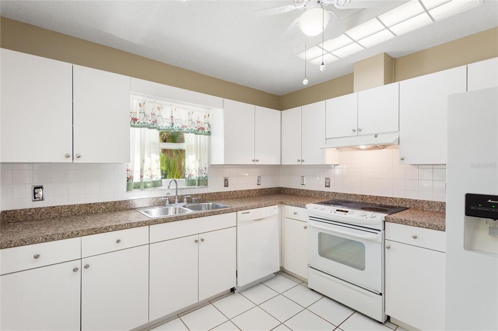 A kitchen with white cabinets, white appliances, a double sink, and speckled brown countertops — 679 FORT DUQUESNA DRIVE, SUN CITY CENTER, FL