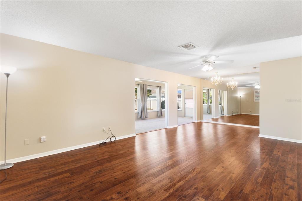 A spacious living room features hardwood floors, beige walls, a ceiling fan, and mirrored walls — 679 FORT DUQUESNA DRIVE, SUN CITY CENTER, FL