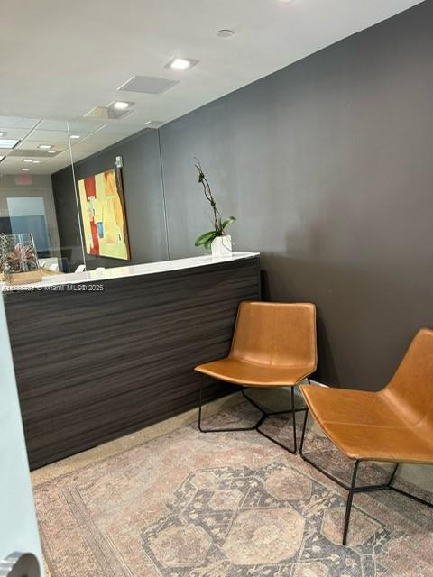 A reception area features a dark wood desk, two tan chairs, and a patterned rug — 95 Merrick Way # 710, Coral Gables FL 33134, CORAL GABLES, FL