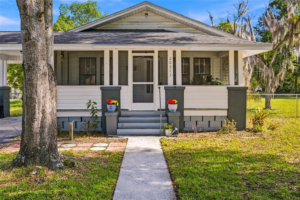 A single-story house with a screened front porch, gray brick accents, and a concrete walkway — 20315 THE GRANADA, DUNNELLON, FL