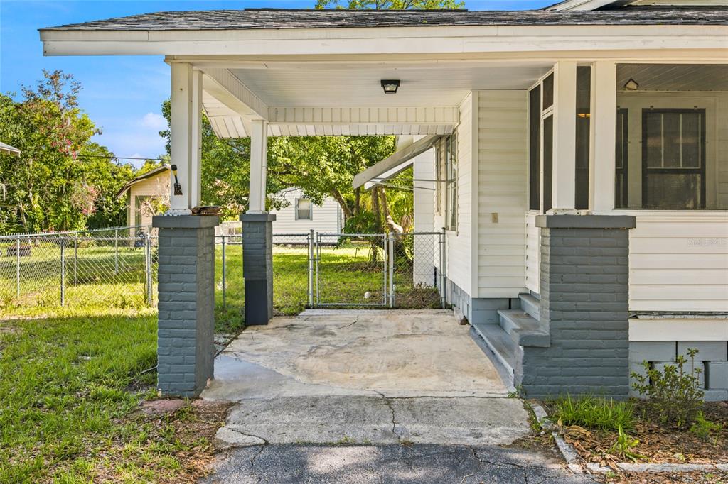 A covered concrete carport with brick pillars sits beside the side entrance of a house — 20315 THE GRANADA, DUNNELLON, FL