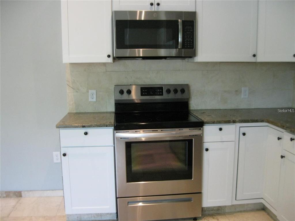 A kitchen features white cabinets, stainless steel appliances, and a stone tile backsplash — 2009 COCOANUT AVENUE UNIT 1, SARASOTA, FL