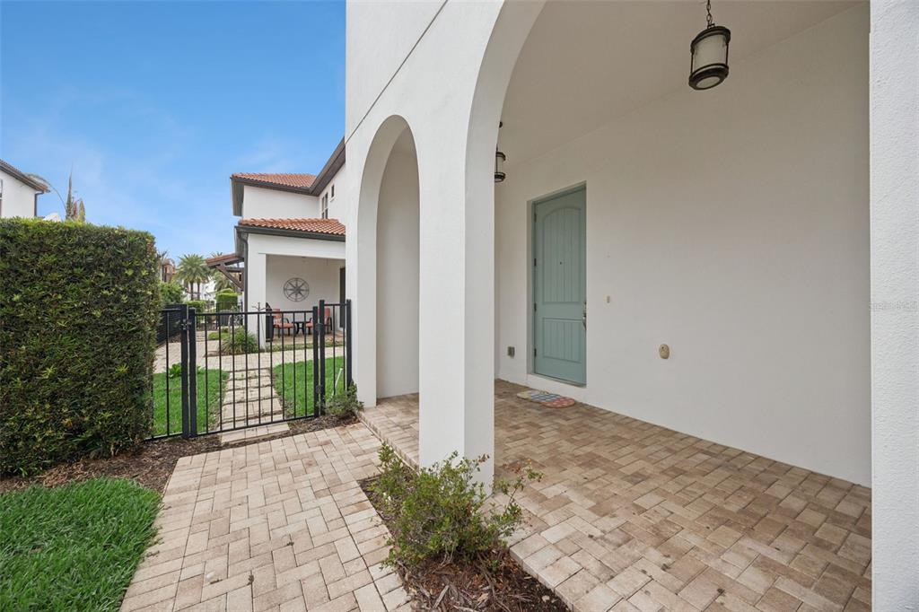 A covered brick patio leads to a light blue front door under a white archway — 8866 BISMARCK PALM DRIVE, WINTER GARDEN, FL
