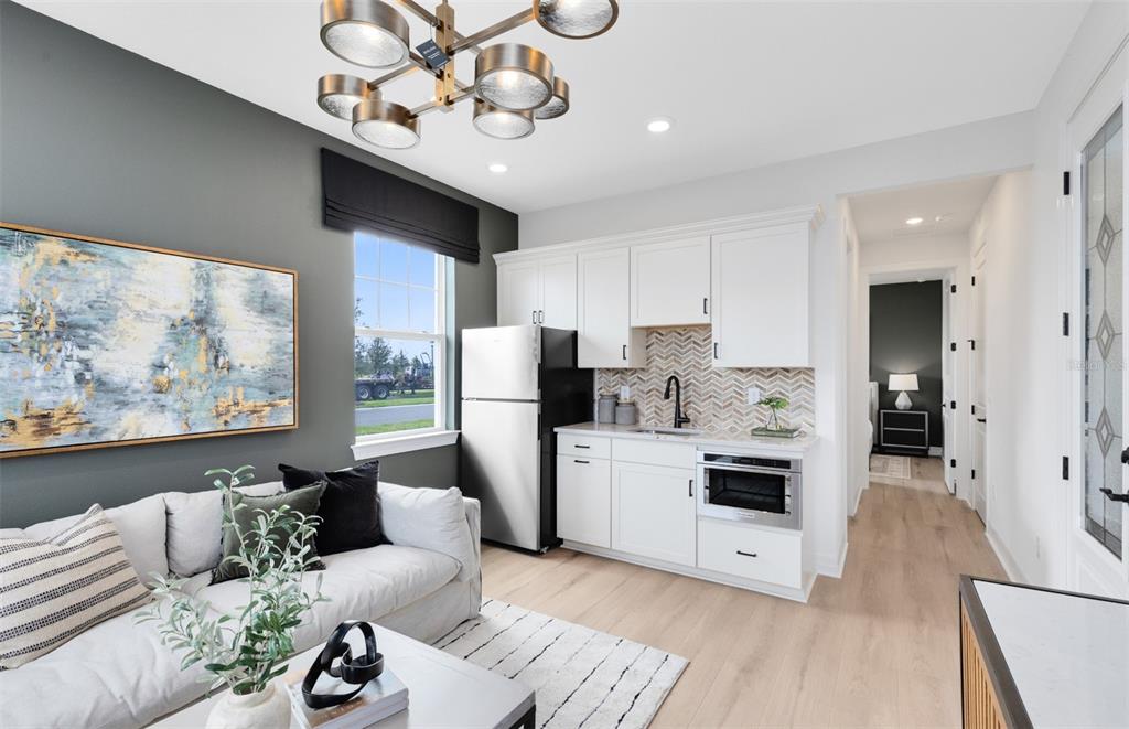 A small kitchenette with white cabinets and a stainless steel refrigerator sits beside a living area — 2627 CLEAR NIGHT AVENUE, KISSIMMEE, FL