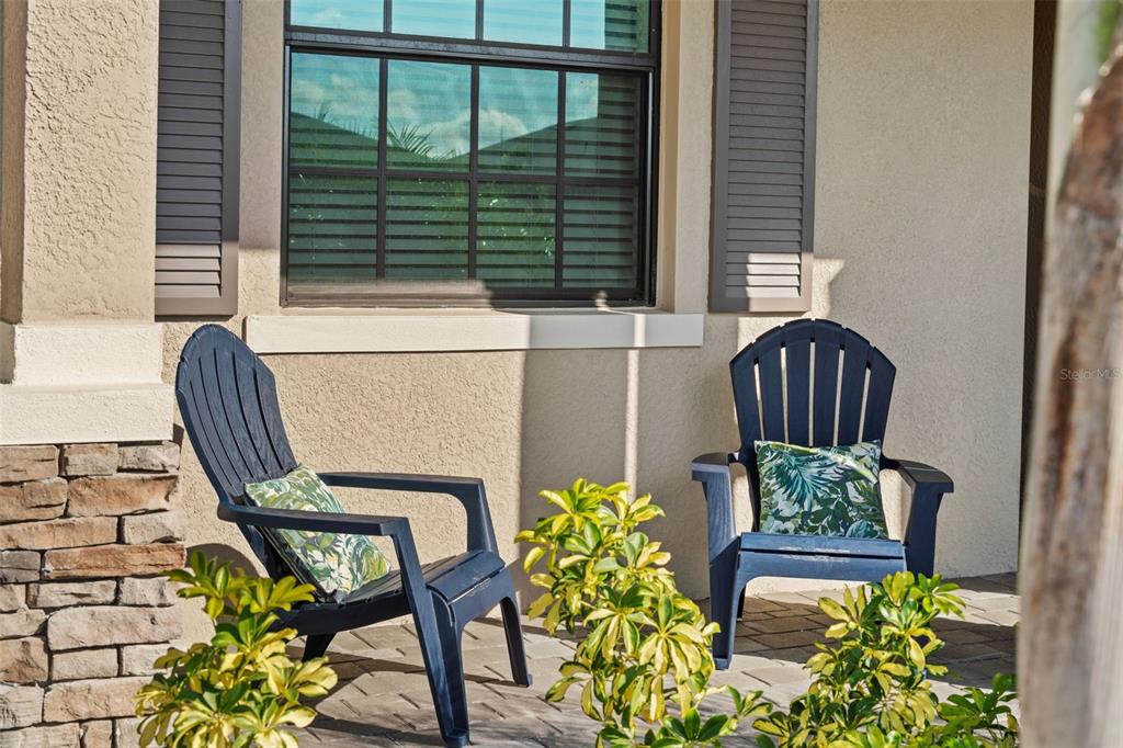 Two dark blue Adirondack chairs with patterned pillows sit on a paved front porch — 1536 SADDLEWOOD CIRCLE, PORT CHARLOTTE, FL