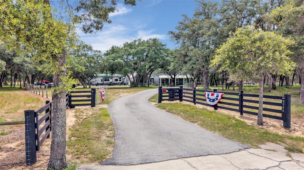 A paved driveway leads through a black wooden fence toward a house surrounded by trees — 8044 LAKE HATCHINEHA ROAD, HAINES CITY, FL